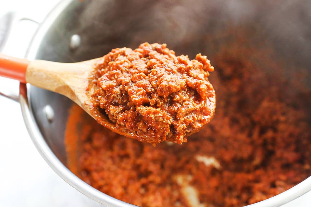 Wooden spoon holding thick chili sauce over a saucepan filled with the mixture.