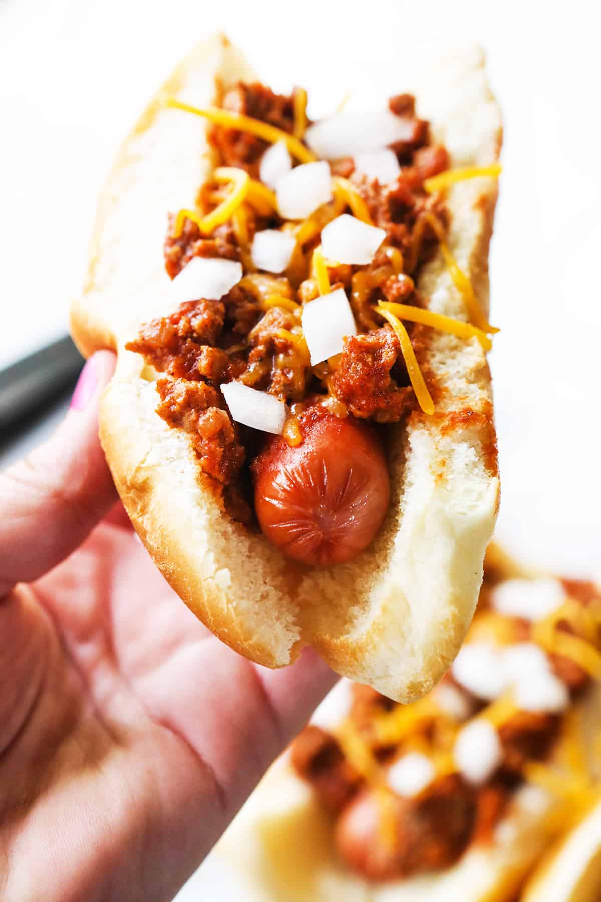 Hand holding a hot dog with chili sauce spread over the top.