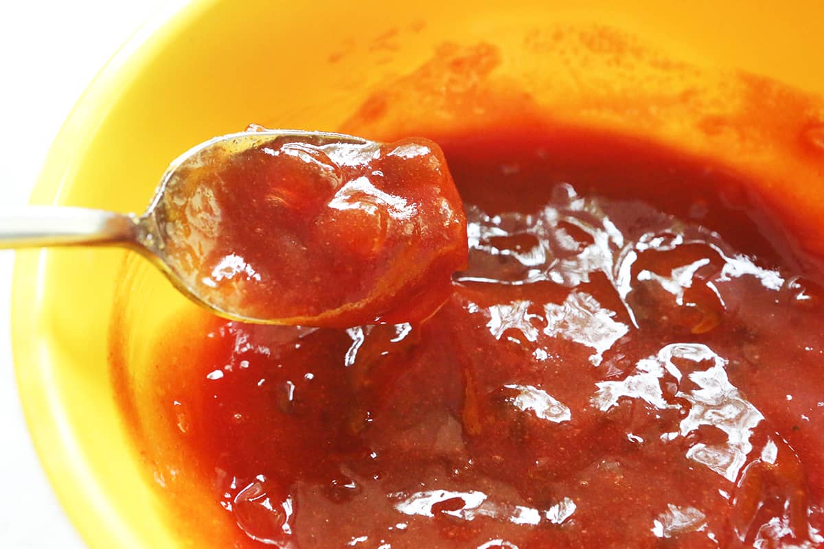 Spoon lifting chunky red sauce out of a bowl.