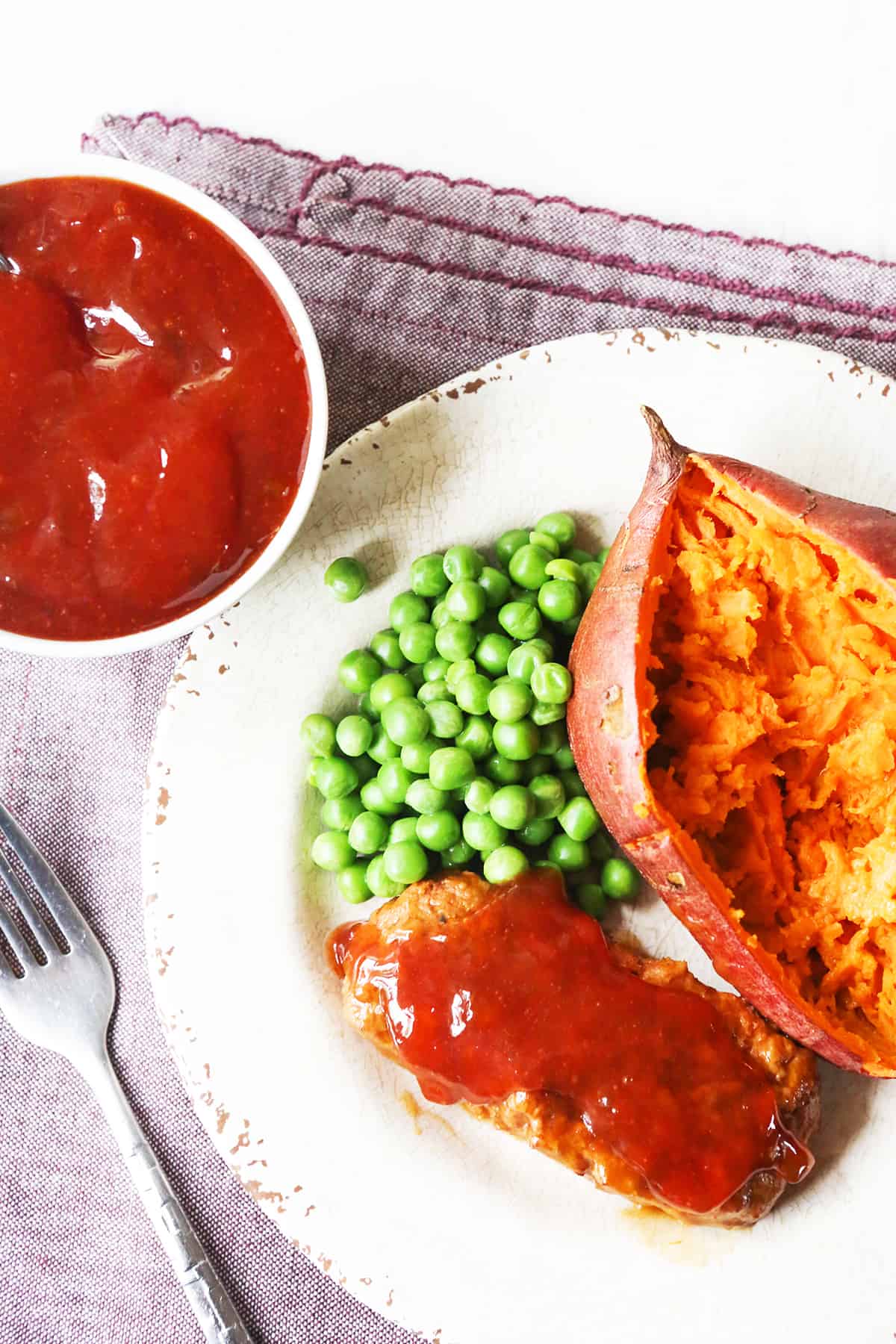 Looking down onto a plate of meatloaf and a potato with red sauce spread over the serving of meatloaf.