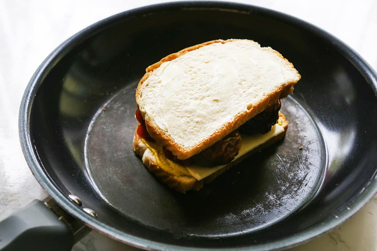 Assembled sandwich in a skillet with butter spread on the outside of the bread.