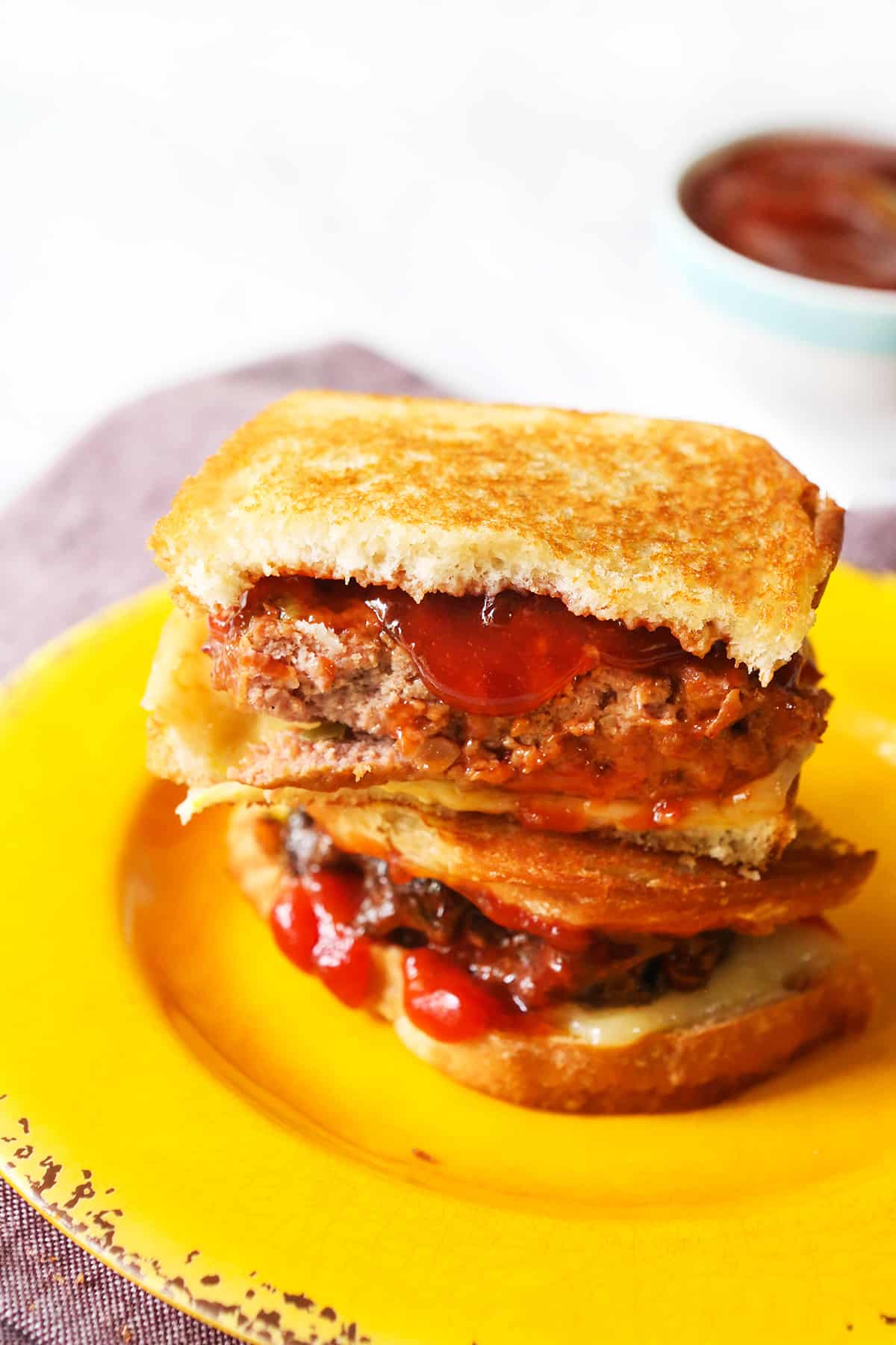 Leftover meatloaf sandwich cut in half and stacked on a yellow plate.