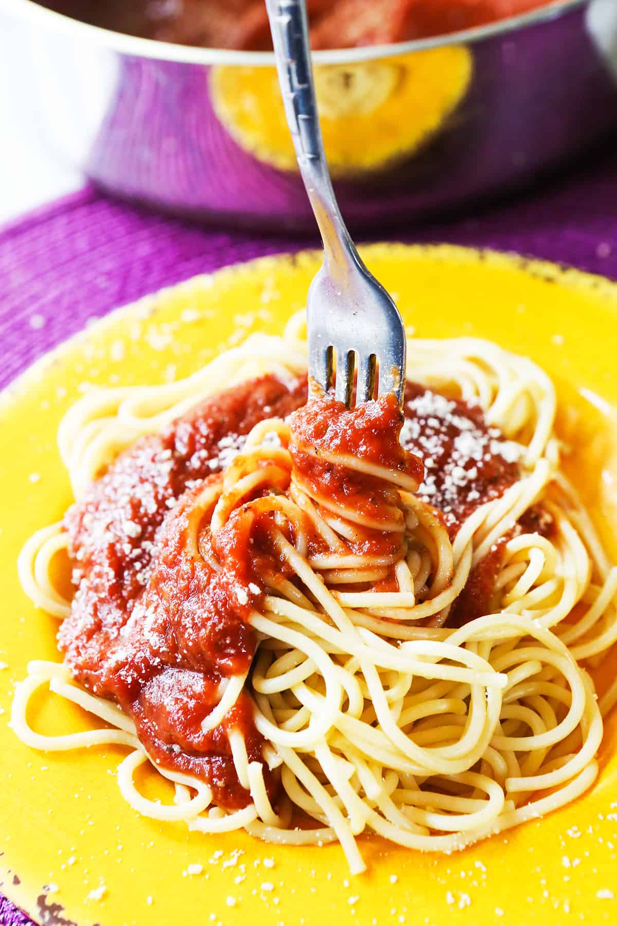 Fork inserted into the center of a heaping pile of spaghetti with sauce.