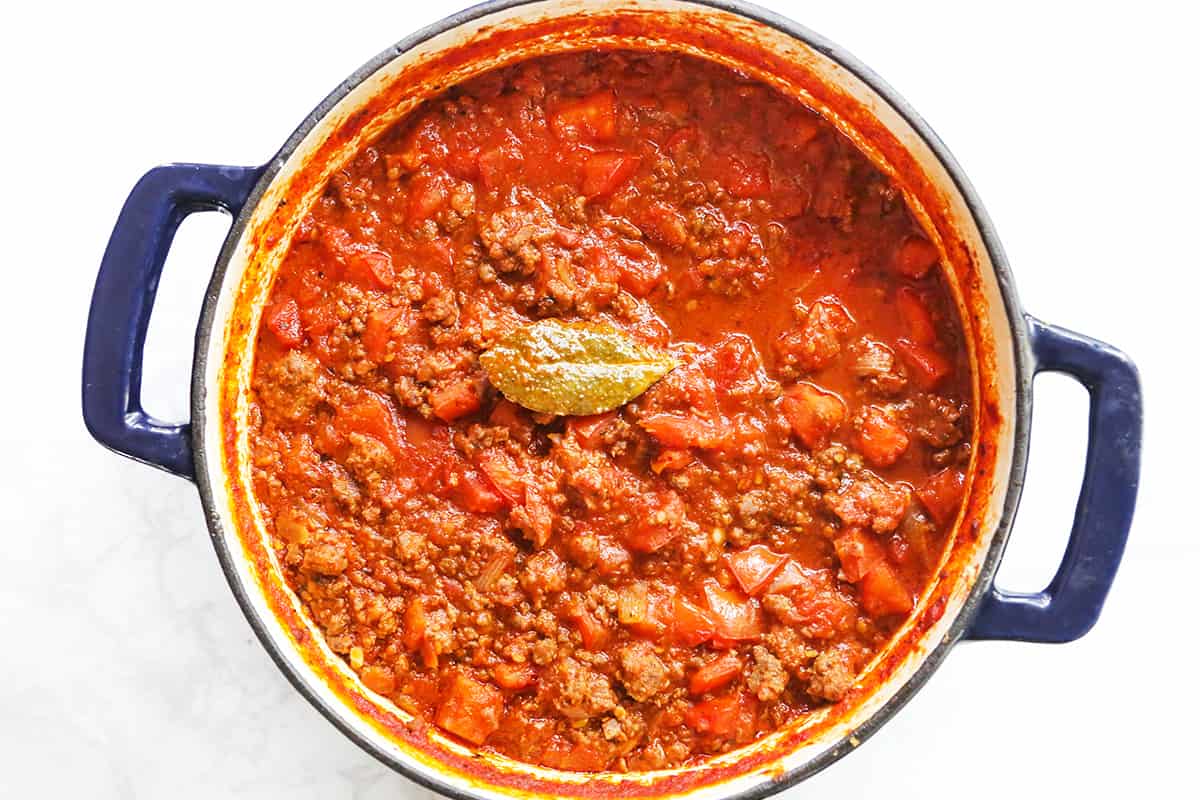 Top view of a Dutch oven filled with meaty pasta sauce and a bay leaf.