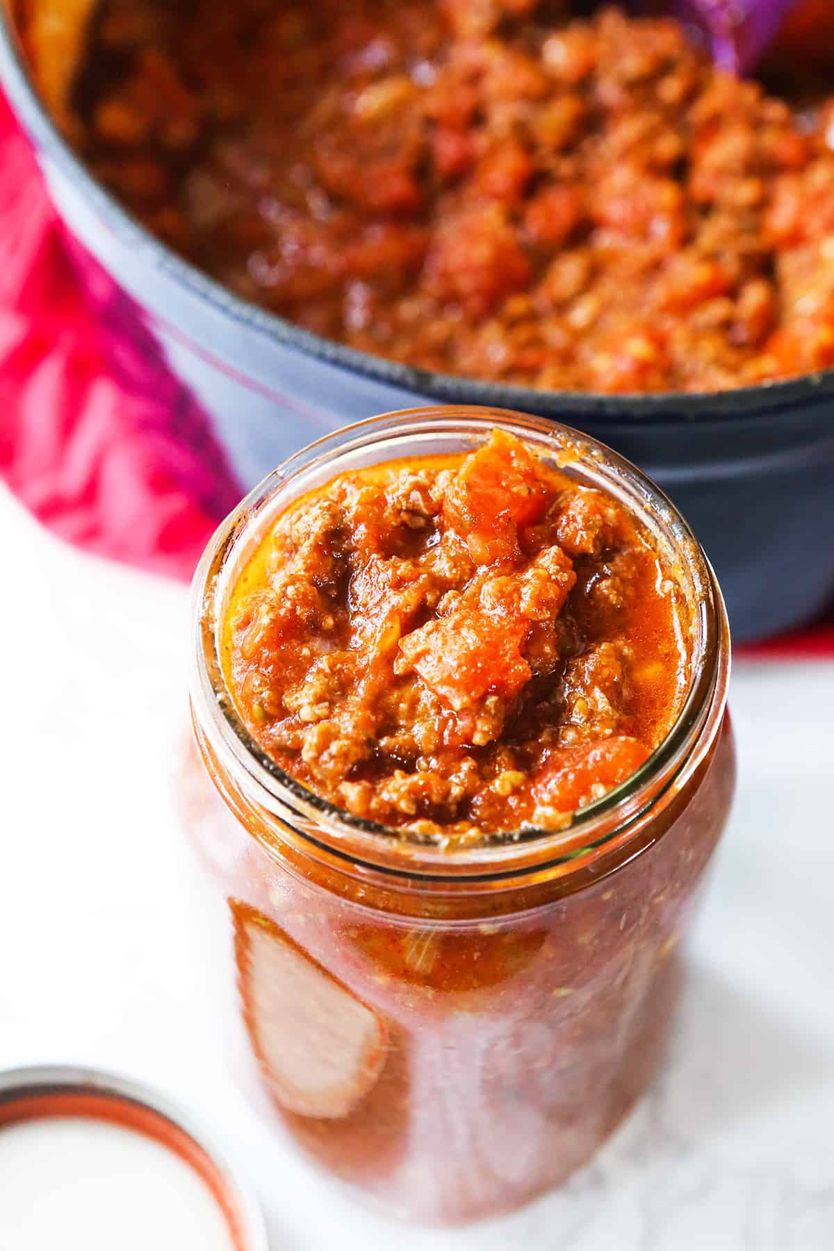 Meaty pasta sauce in a mason jar, sitting next to a pan filled with the same sauce.
