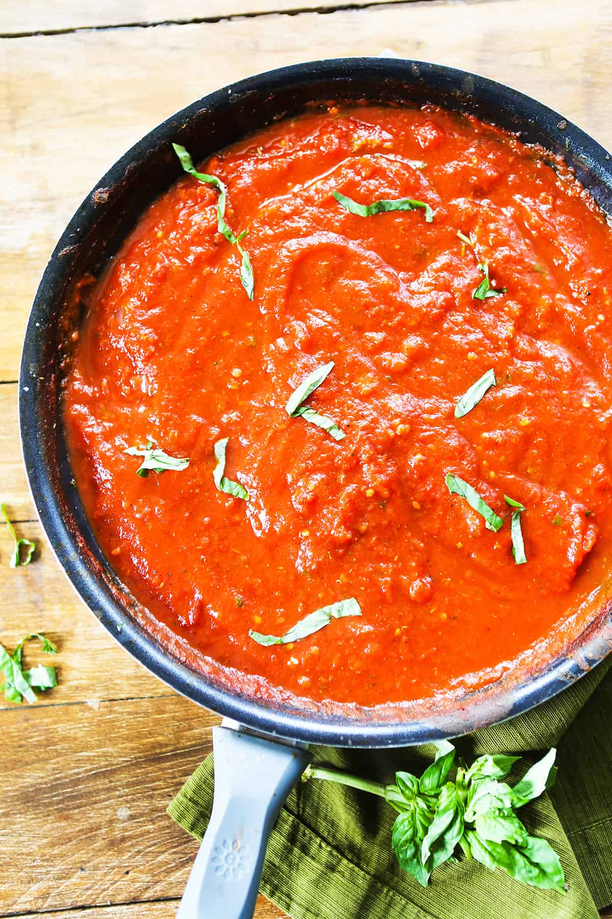 Top view of a skillet filled with marinara sauce, with fresh basil sprinkled on top.