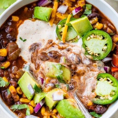 Black bean vegetarian chili with spiced yogurt in the bowl with chunks of avocados and sliced jalapenos. 