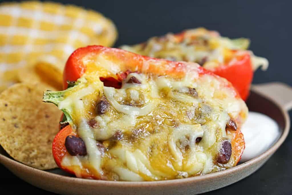 Half of a red pepper stuffed with leftover chili and melted cheese over it on a plate with some tortilla chips. 