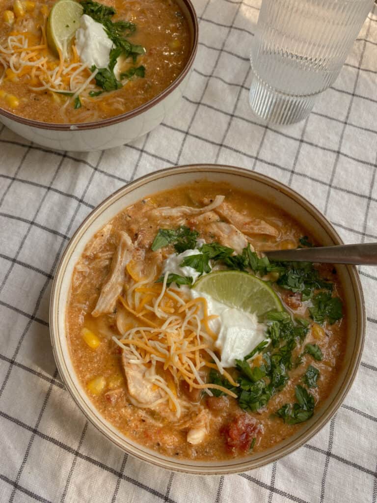 Spoon in a bowl of instant pot white chicken chili garnished with cilantro and lime wedges. 