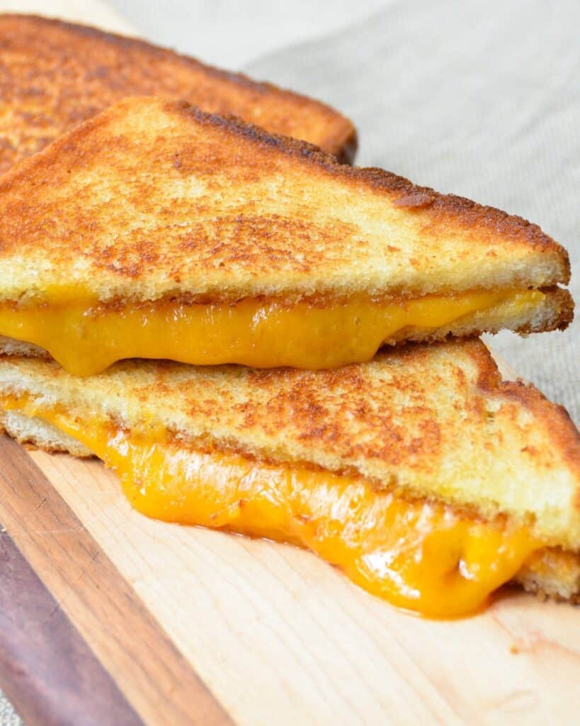 Halved grilled cheese sandwiches with cheese oozing out on a plate. 