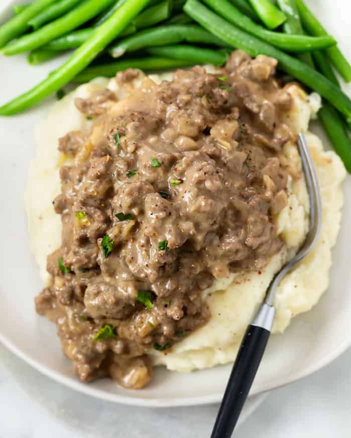 Hamburger gravy over potatoes with a side of green beans on the plate. 