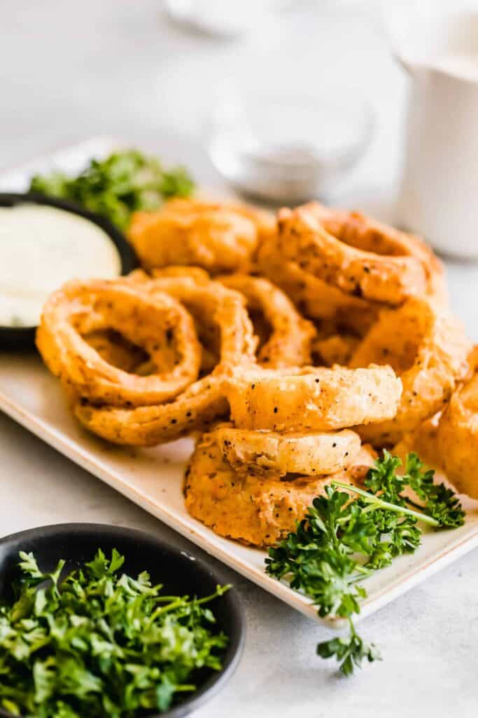 Lots of onion rings on a plate with parsley as garnish. 