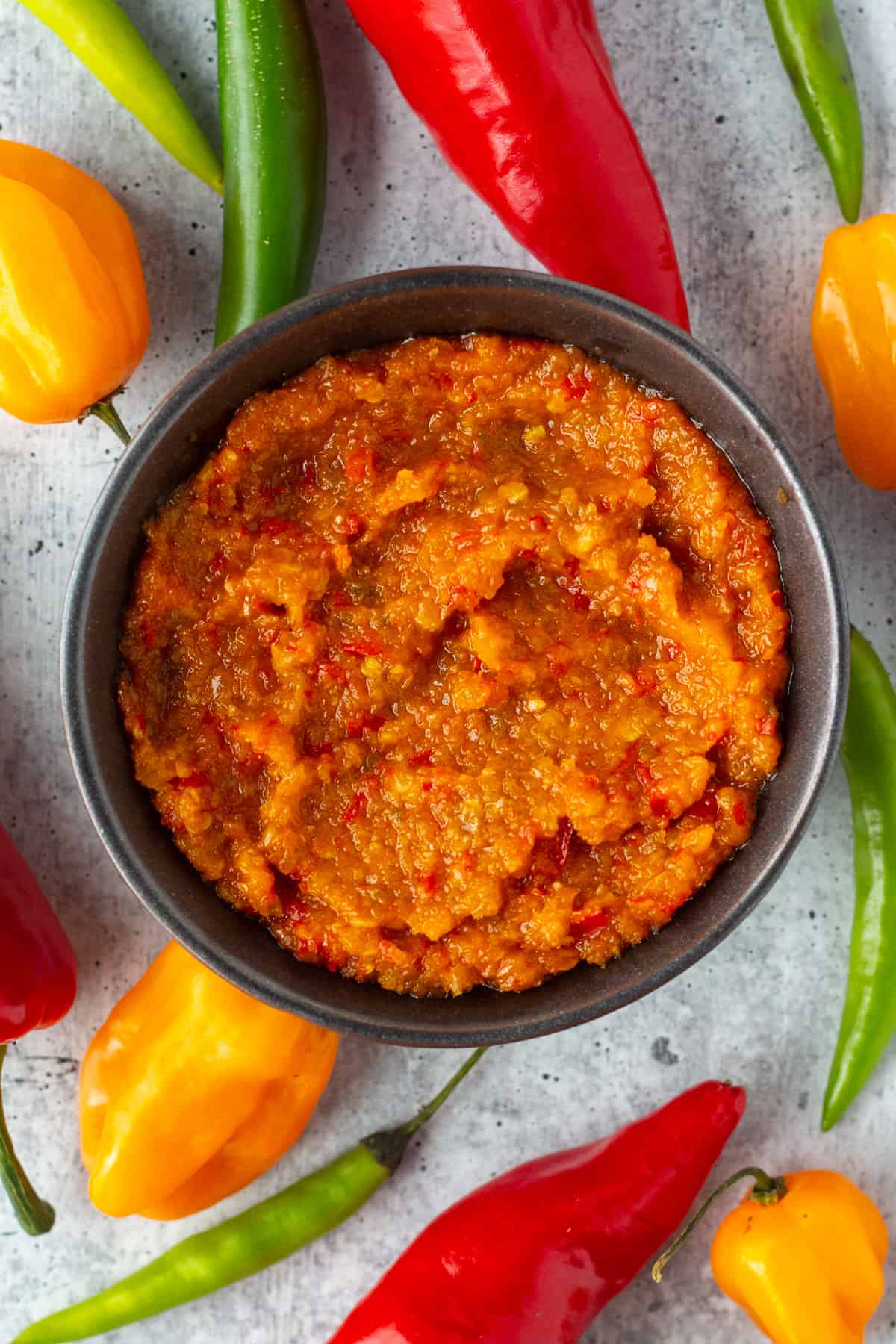 Top view of a bowl of chili paste surrounded by colorful peppers.