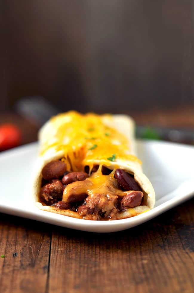 One cheesy leftpver chili stuffed burrito on a plate. 