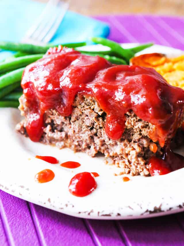 Slice of meatloaf with red sauce covers the top with a side of green beans. 