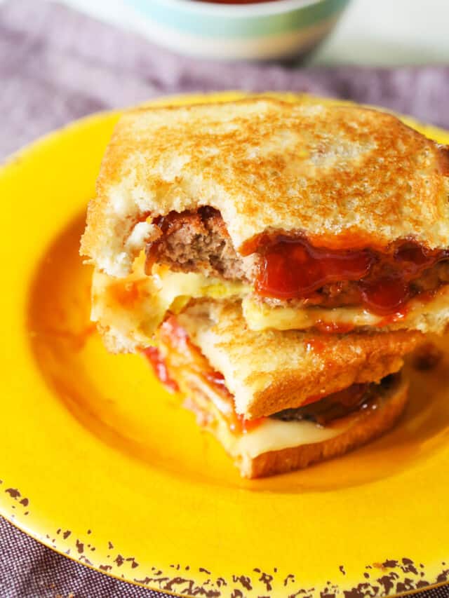 Meatloaf sandwich on a yellow plate with one bite removed.