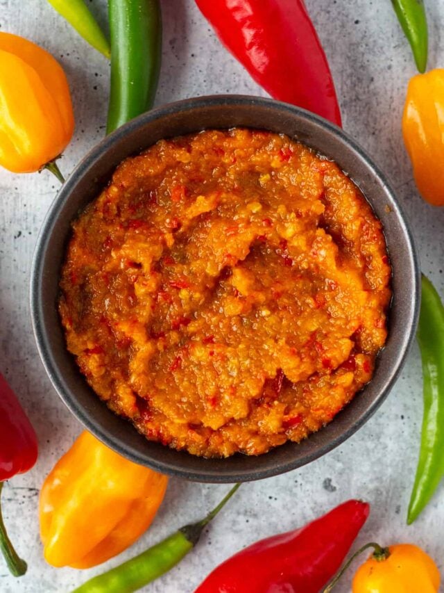 Bowl filled with chili paste, surrounded by colorful peppers.
