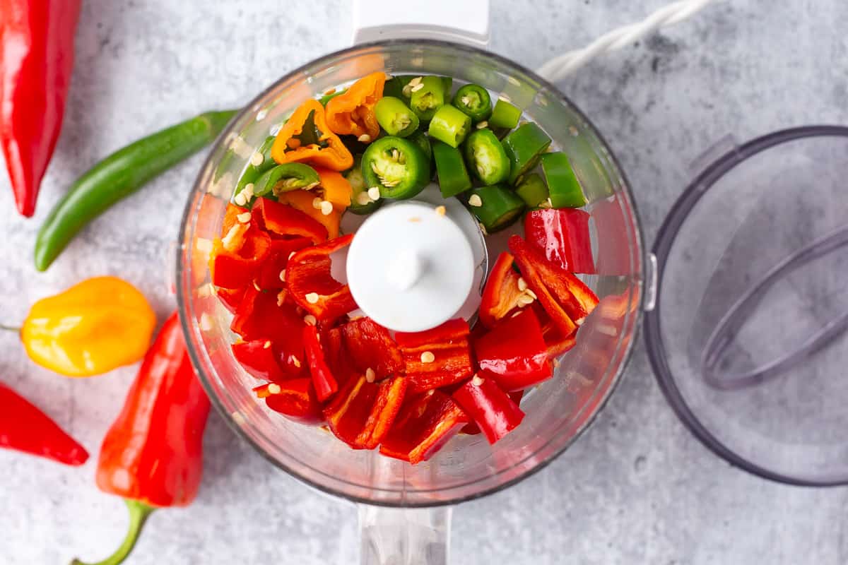 Top view of food processor filled with chopped colorful peppers.