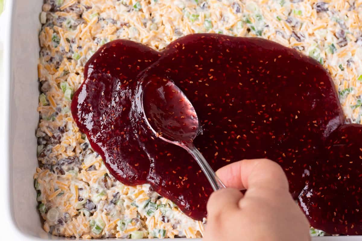 Close-up of raspberry dip being spread over a creamy salad or dip.
