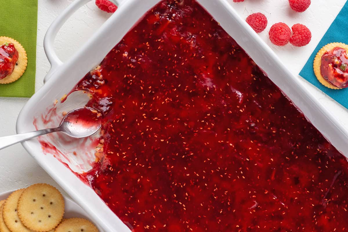 Close-up of vibrant raspberry dip in a white dish with cookies and berries.