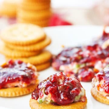 Raspberry dip served on crackers with fresh berries and cookies in the background.