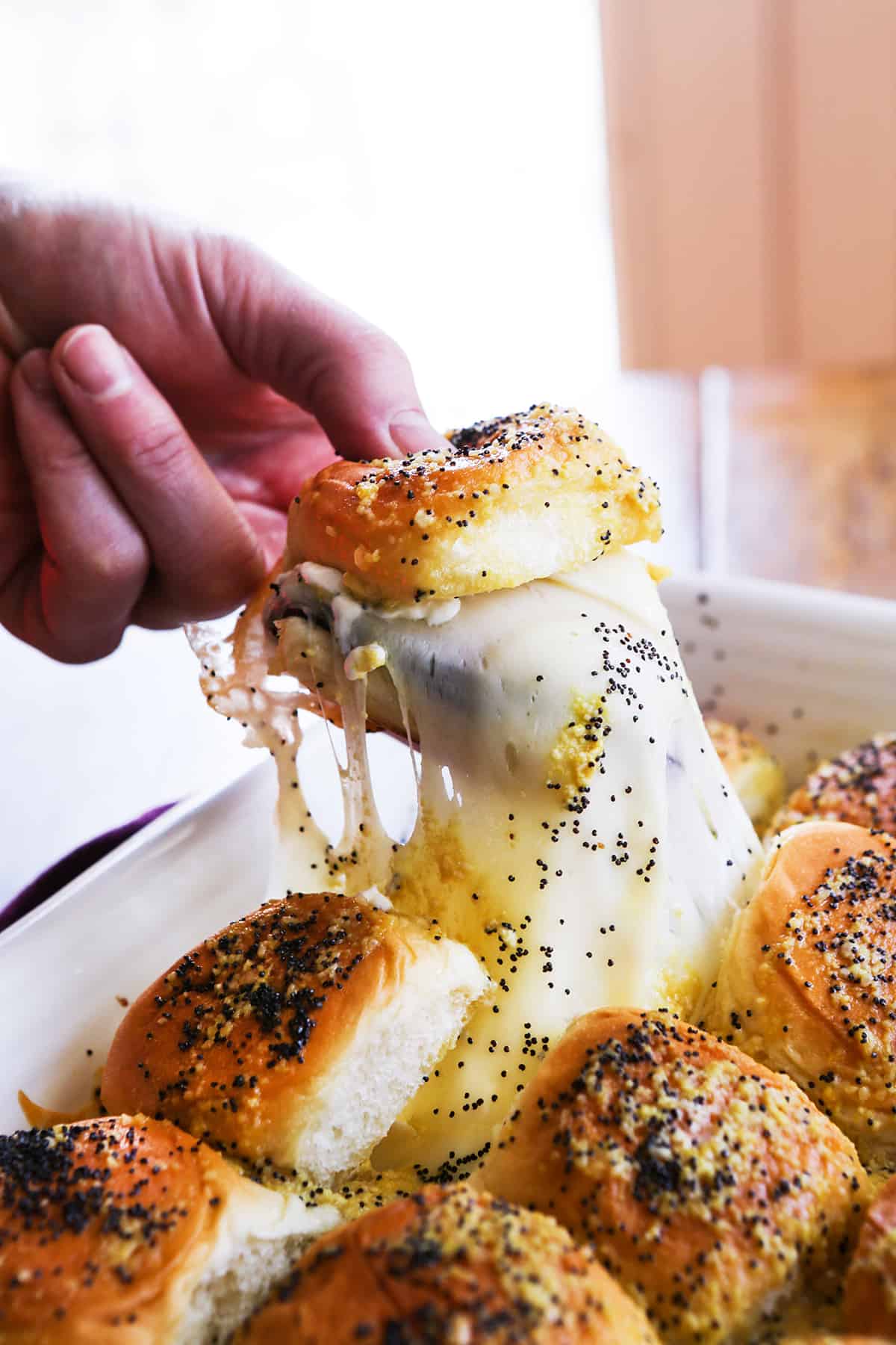 Hand pulling a cheesy ham sandwich out of a baking dish.