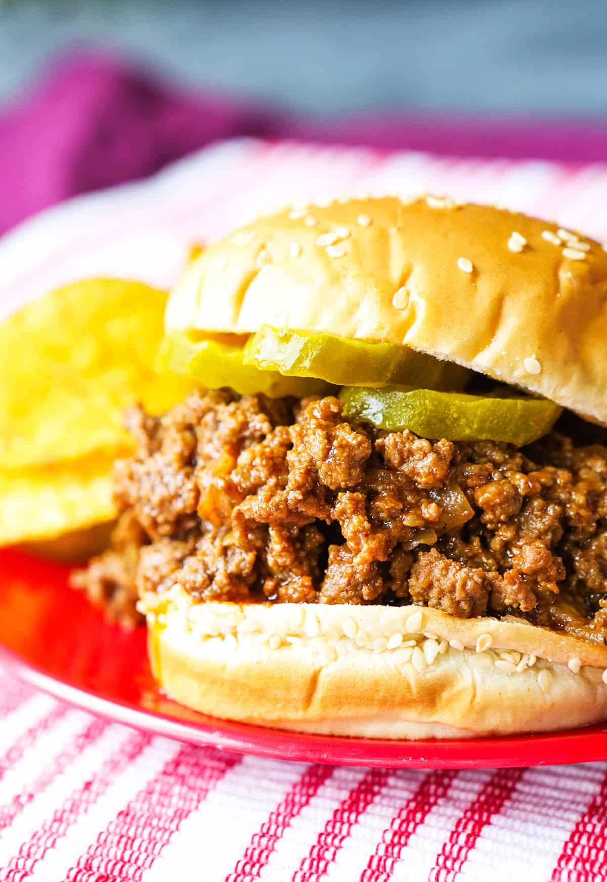 Close up of a loaded sloppy joe sandwich, sitting next to chips on a plate.