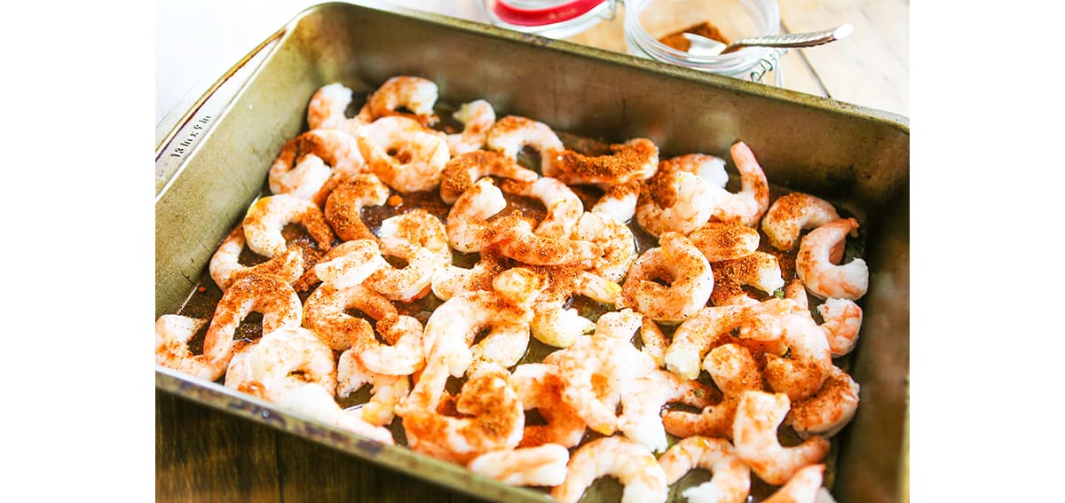 Shrimp in a single layer in baking pan, topped with seasoning.
