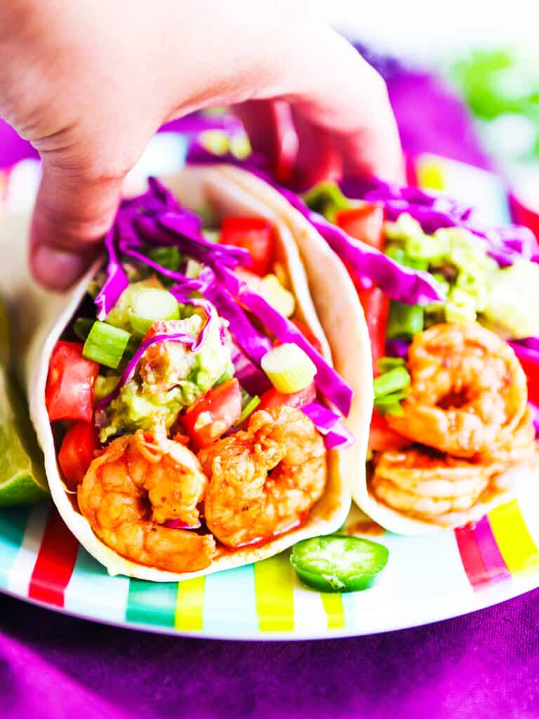 Hand picking up a shrimp taco with cabbage and garnished with green onions and tomatoes. 