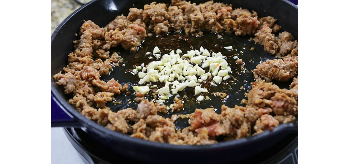 Skillet with cooked ground meat and minced garlic in the center.