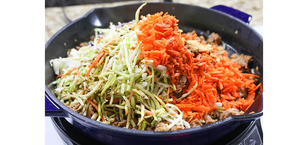 Heaping pile of shredded carrots and coleslaw mix in a skillet.