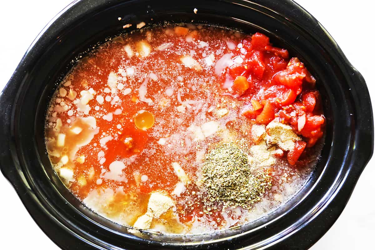 Diced tomatoes, seasonings and other liquids in a slow cooker.