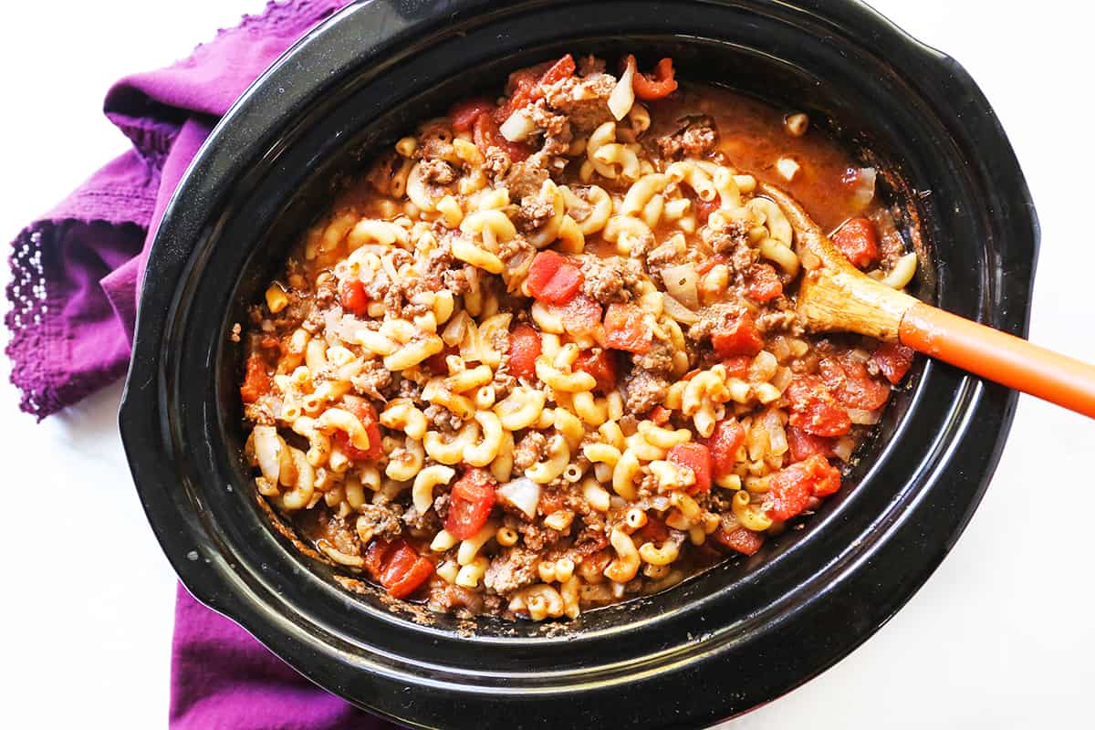Goulash in a slow cooker with a wooden spoon in it. 