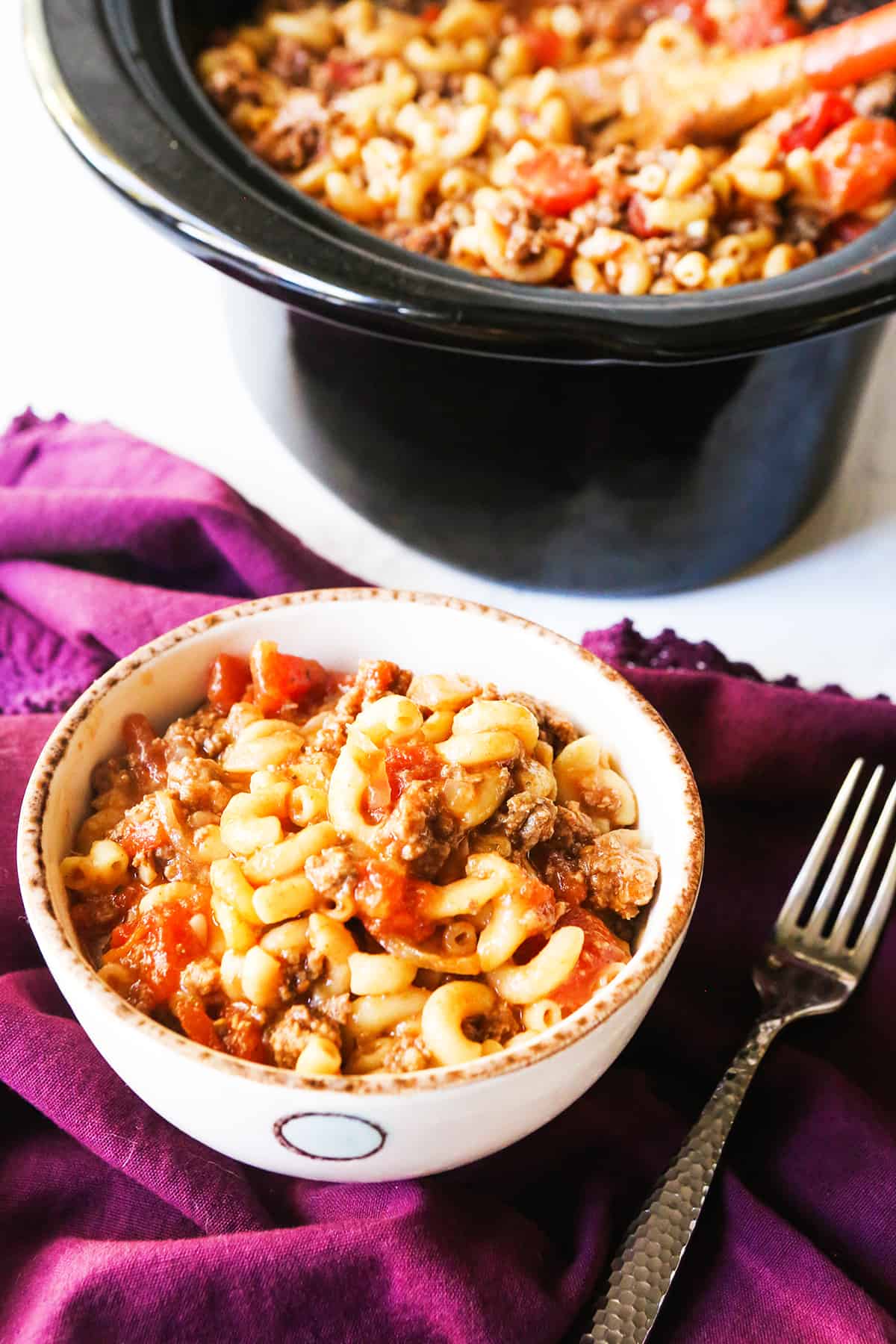 Bowl of goulash sitting next to a pot of it.