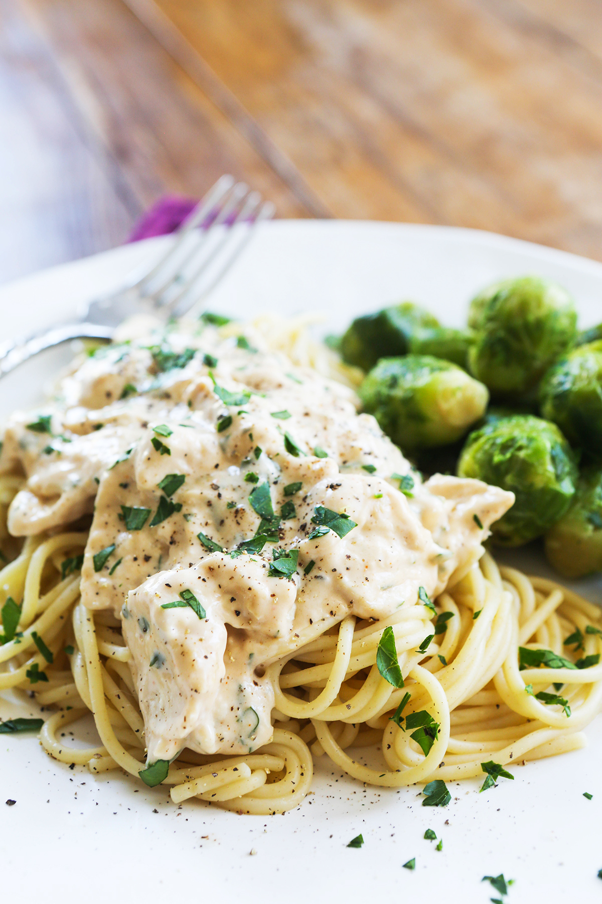 Plate of cooked pasta with alfredo sauce and chicken, next to cooked Brussels sprouts.