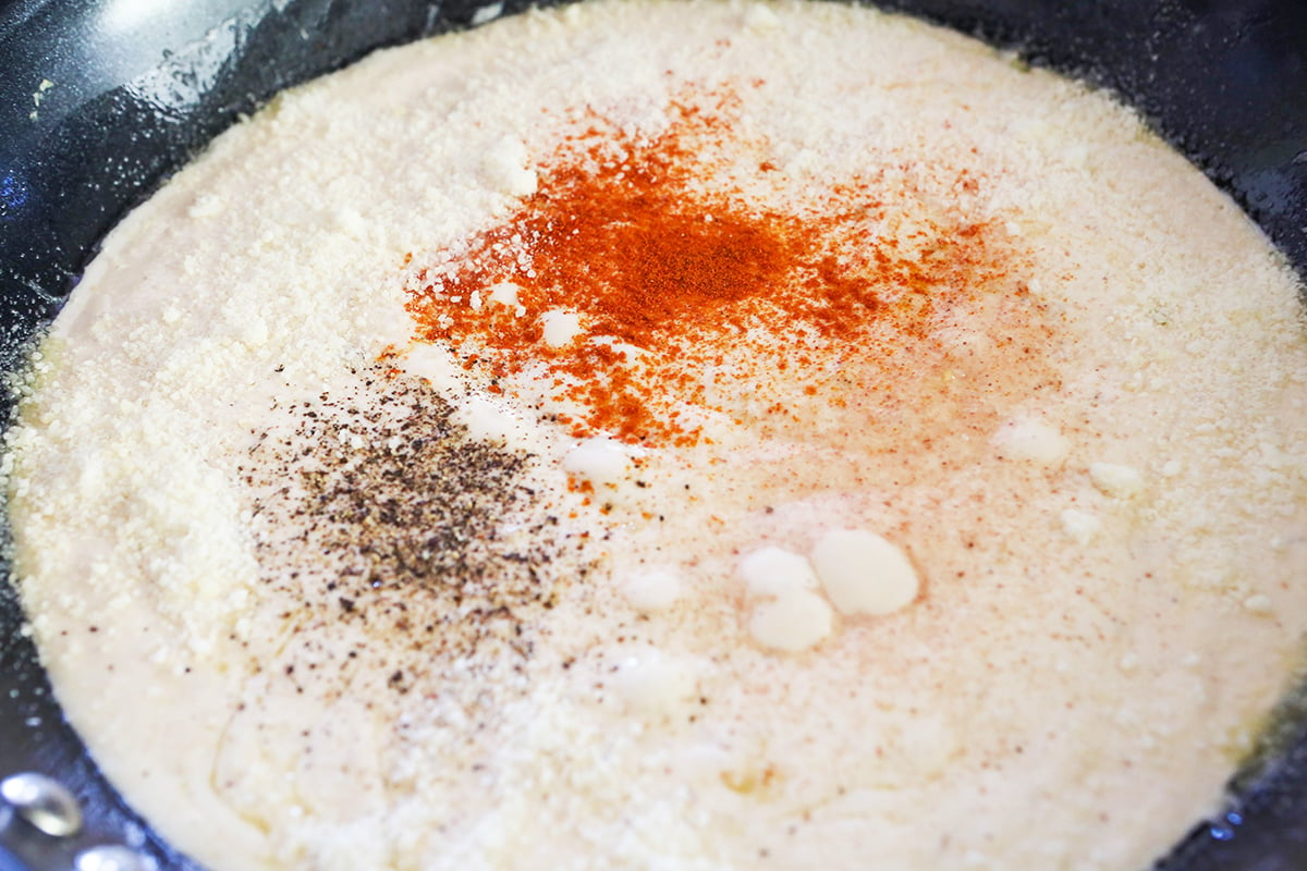 Seasonings on top of alfredo sauce in a skillet.
