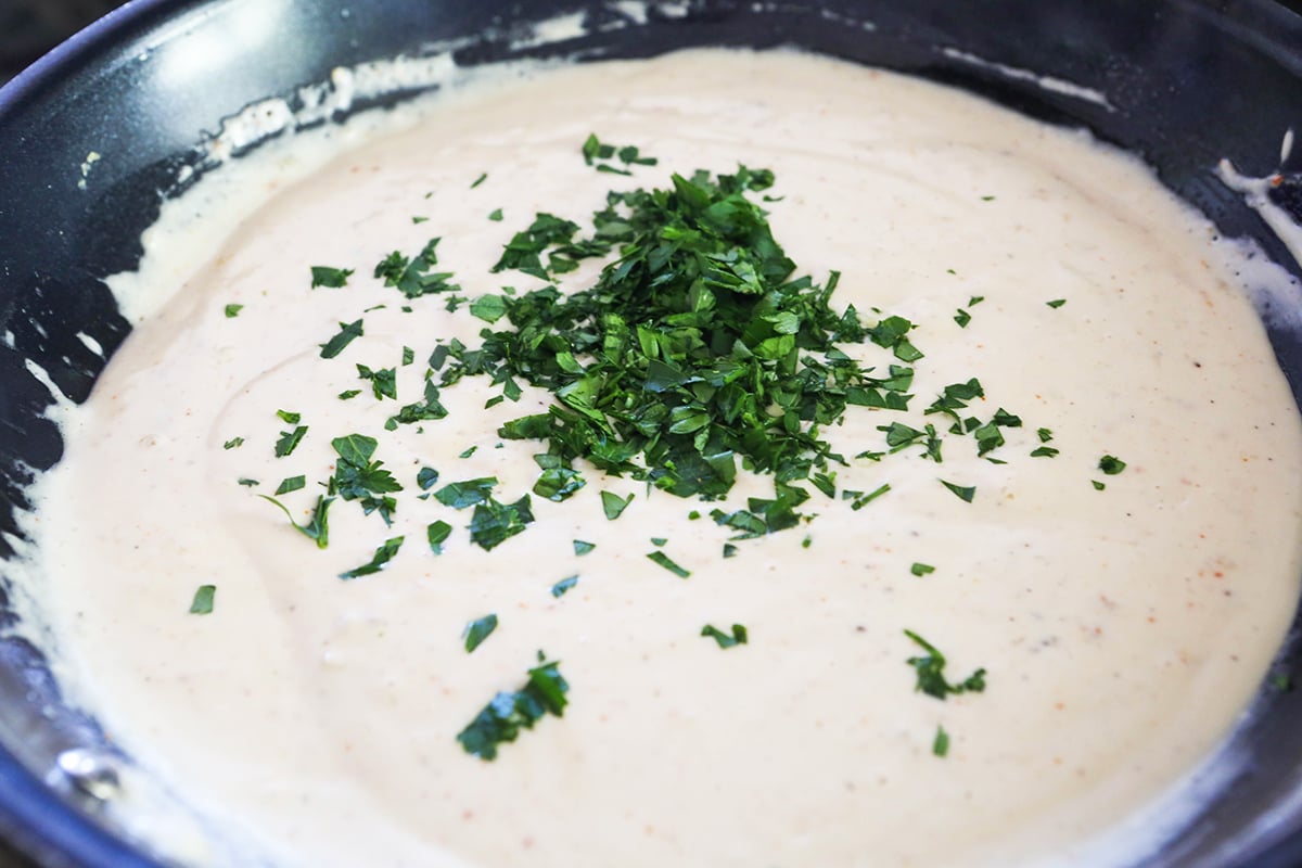 Chopped parsley in a small pile on alfredo sauce.