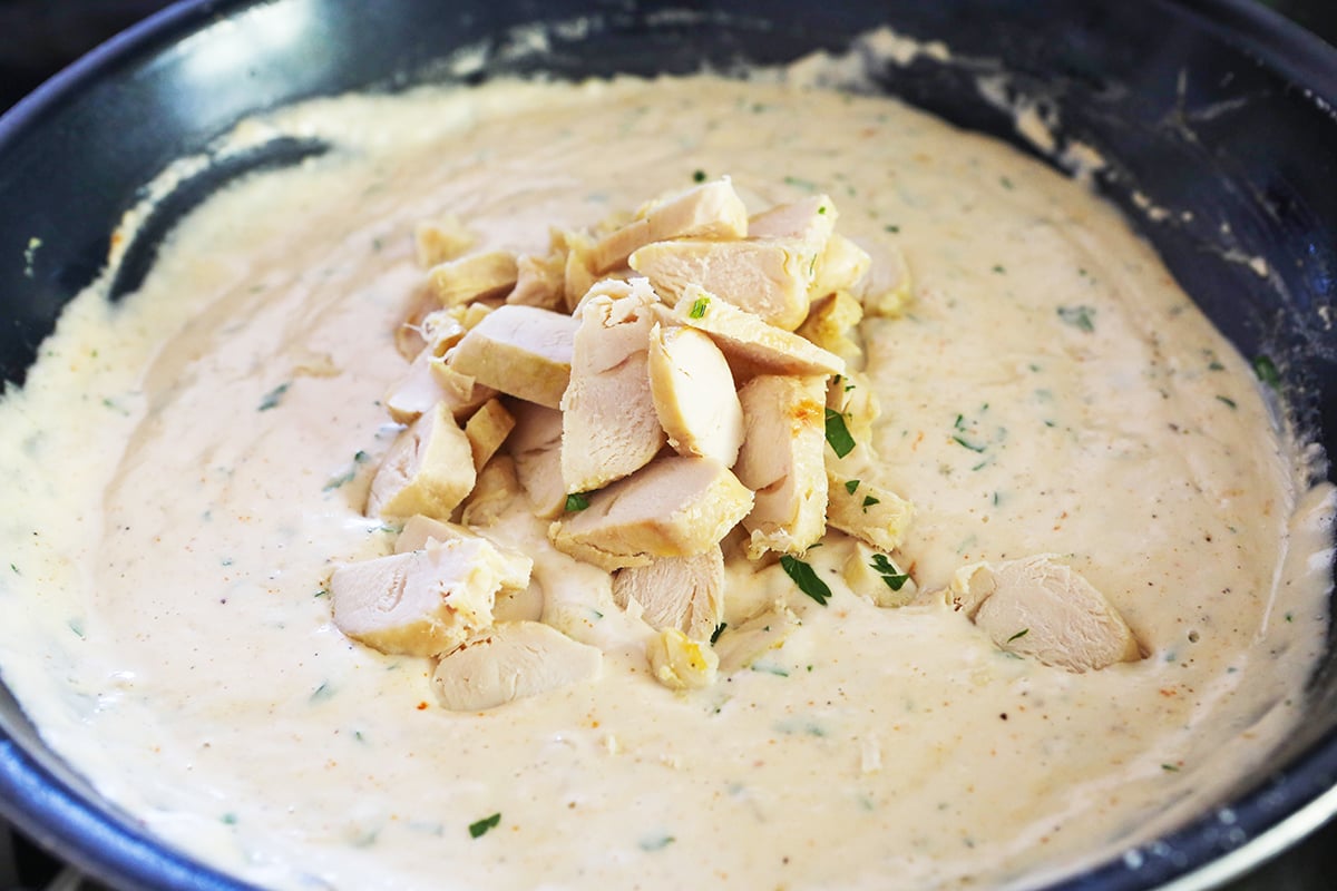 Alfredo sauce in a skillet with cooked chicken pieces sitting on top.