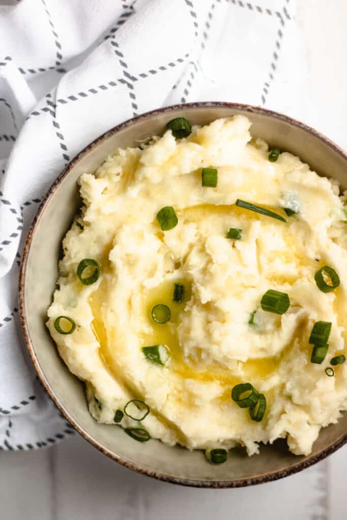 Serving bowl of horseradish mashed potatoes and green onions garnished on top. 