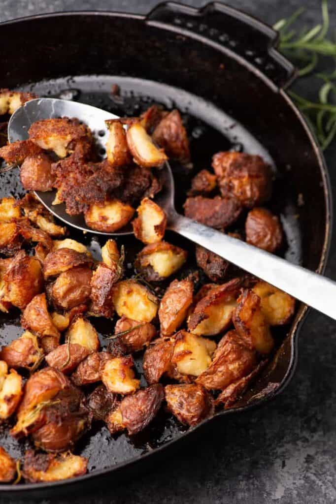 Cast iron skillet with a serving spoon holding crunchy roasted potatoes. 