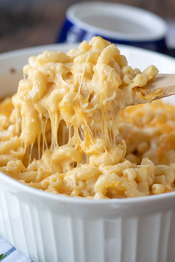 Wooden spoon filled with gooey mac and cheese coming out of the baking dish.