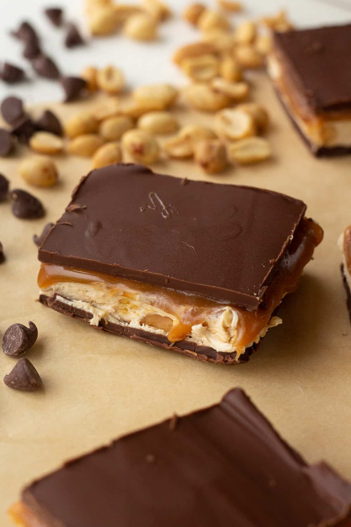 One piece of fudge on parchment, surrounded by peanuts and chocolate chips.