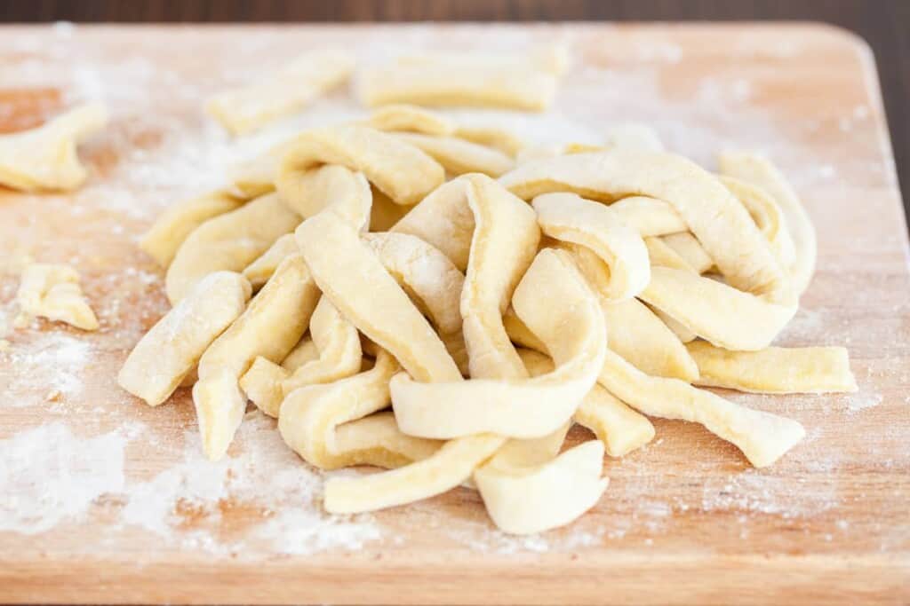 Homemade egg noodles sitting on a cutting board over a dusting of flour.