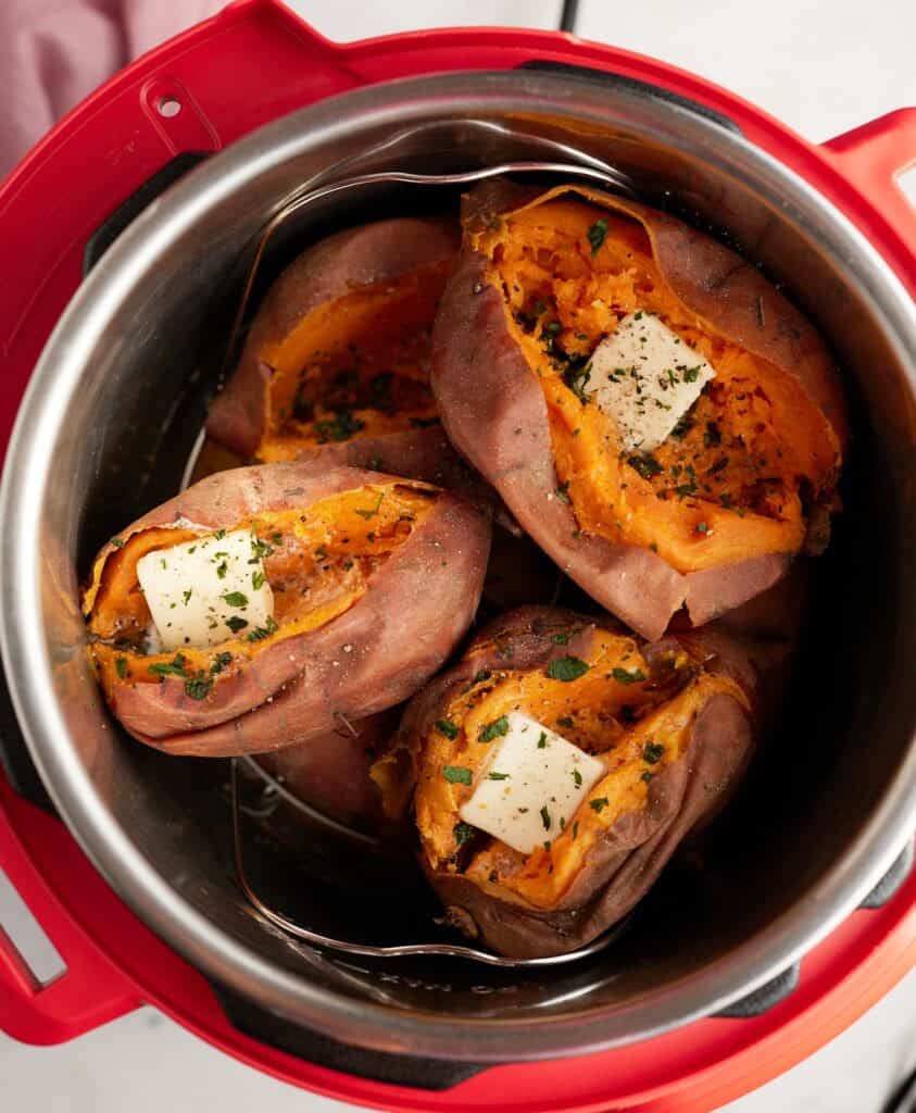 Top view looking into an instant pot of cooked sweet potatoes with a pat of butter in each. 