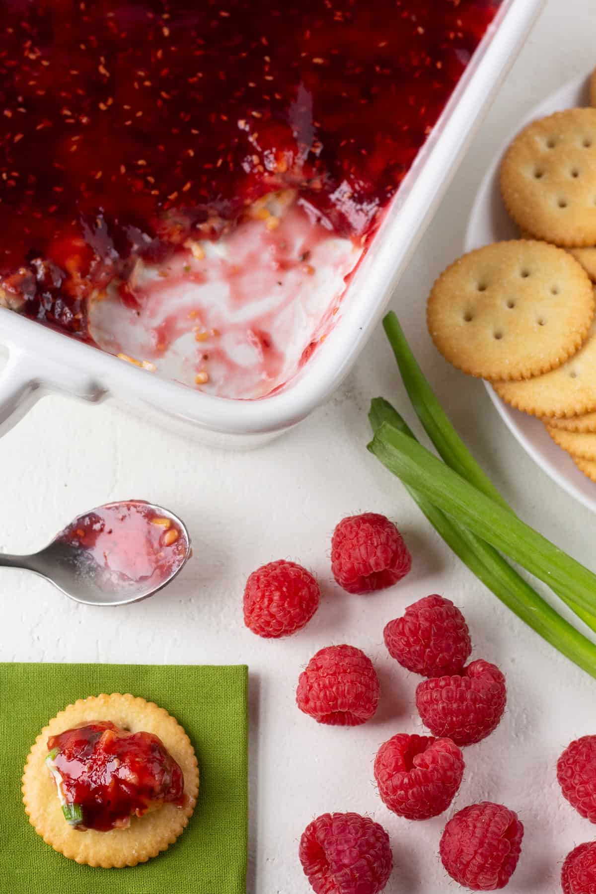 Raspberry dip in a pan sitting next to crackers and raspberries.