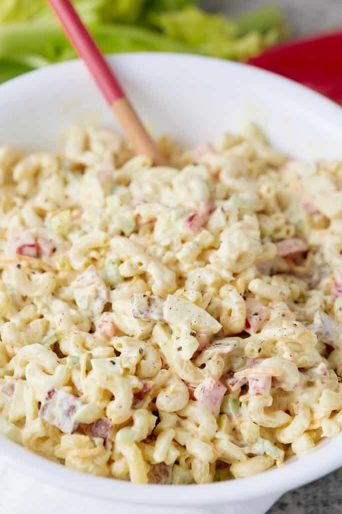 Bowl of macaroni salad with a wooden serving spoon tucked inside. 