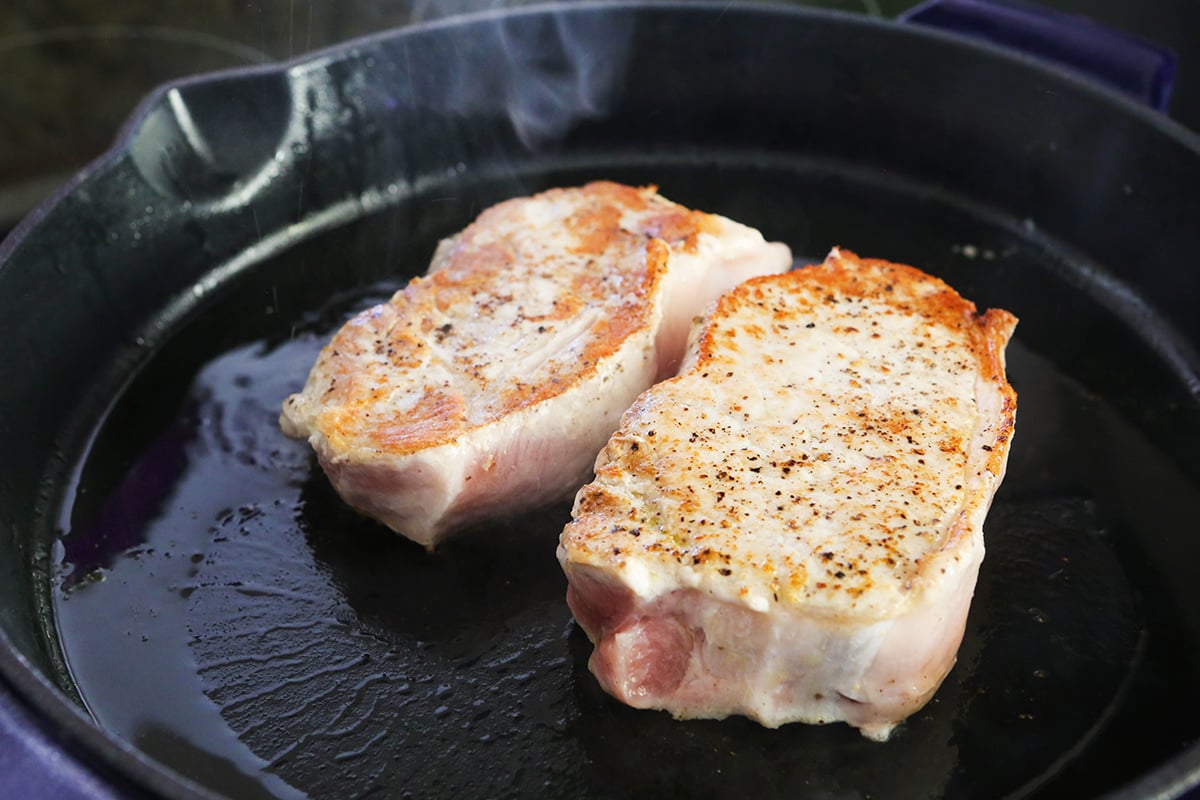 Close up of two seared pork chops sitting in a skillet.