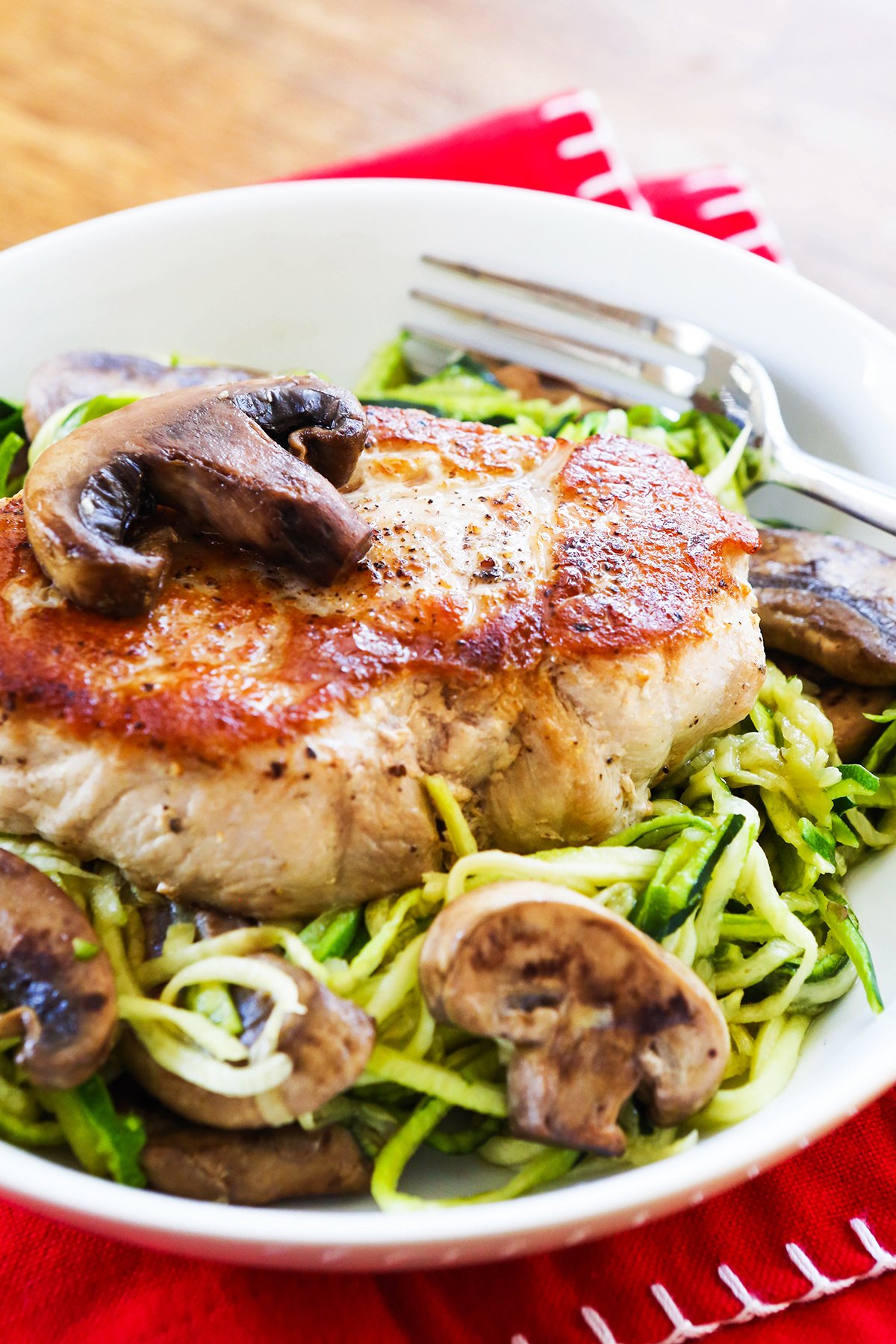 Plate of zoodles topped with a pork chop and sauteed mushrooms.