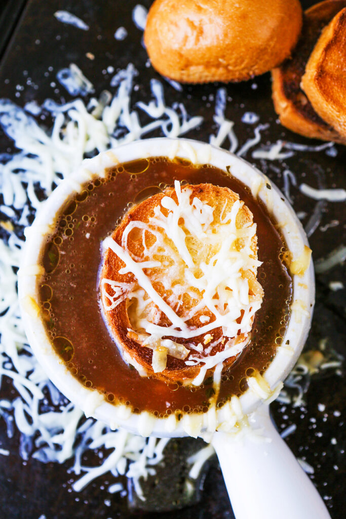 Soup bowl with french onion soup and a crouton with melted cheese floating in it. 