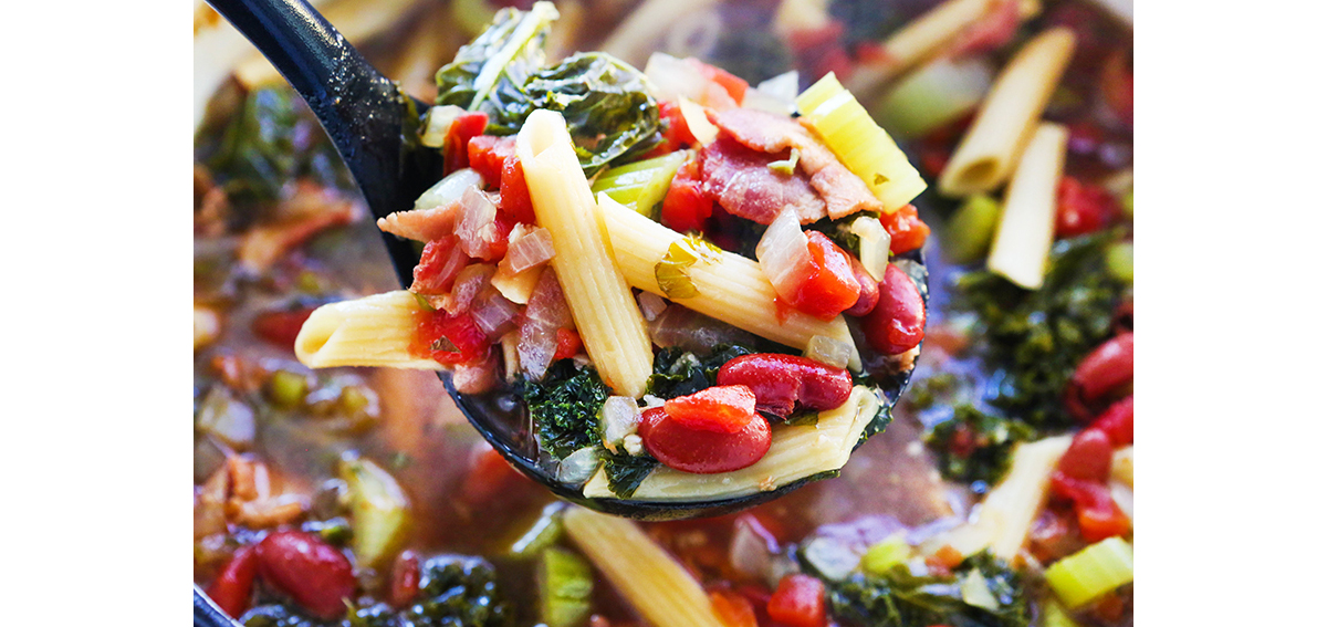 Ladle filled with minestrone soup.